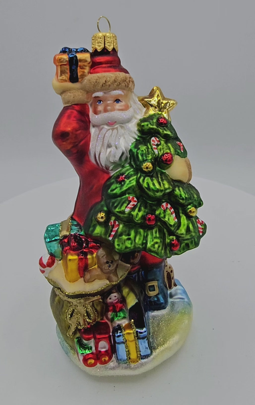 Eine weihnachtskugel dreht sich auf Teller. Ein Weihnachtsmann hält einen Baum im Arm und viele Pakete und Spielzeug stehen vor ihm