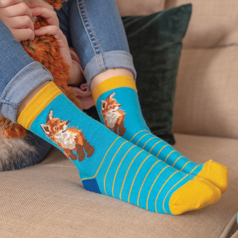 Person mit blauen Motivsocken und Sportschuhen sitzt entspannt auf einem Holzsteg am See